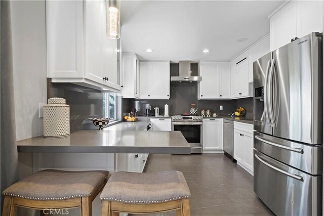 kitchen featuring a kitchen breakfast bar, wall chimney exhaust hood, appliances with stainless steel finishes, decorative light fixtures, and white cabinetry