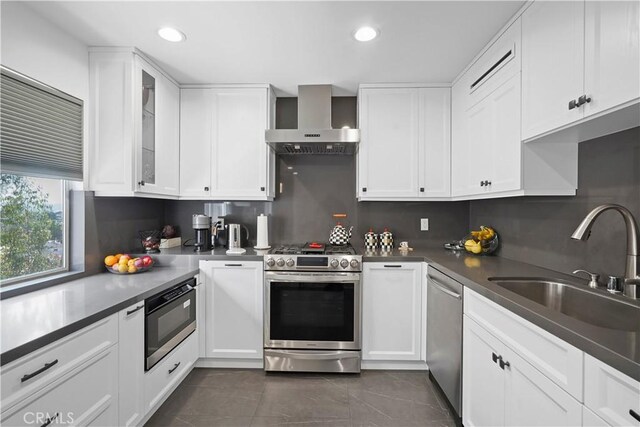 kitchen with appliances with stainless steel finishes, tasteful backsplash, sink, wall chimney range hood, and white cabinetry