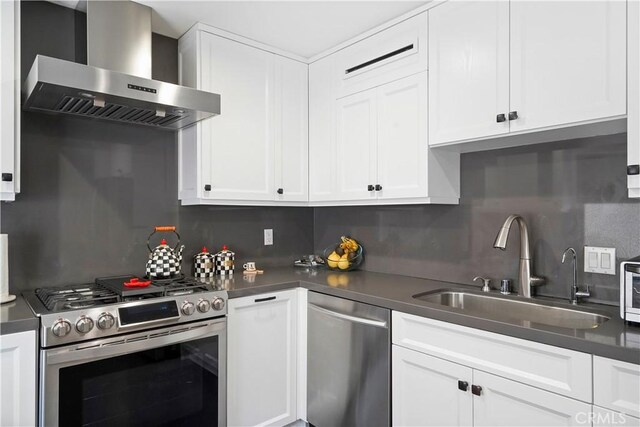 kitchen featuring wall chimney range hood, sink, decorative backsplash, white cabinetry, and stainless steel appliances