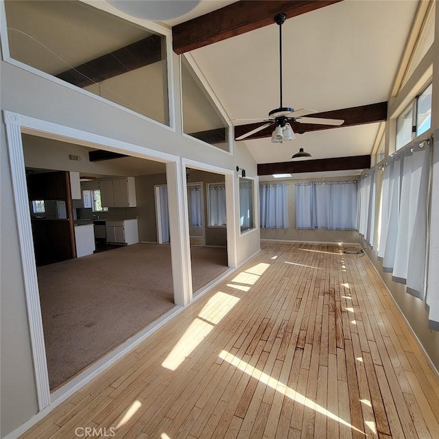 unfurnished sunroom featuring vaulted ceiling with beams, ceiling fan, and a healthy amount of sunlight