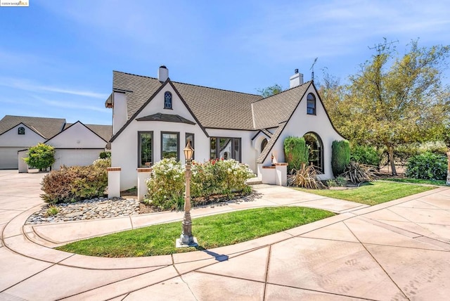 english style home featuring a garage and a front lawn