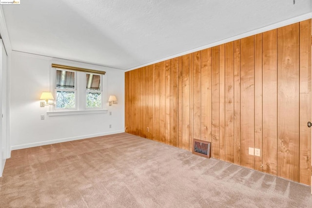 carpeted spare room with crown molding and wooden walls