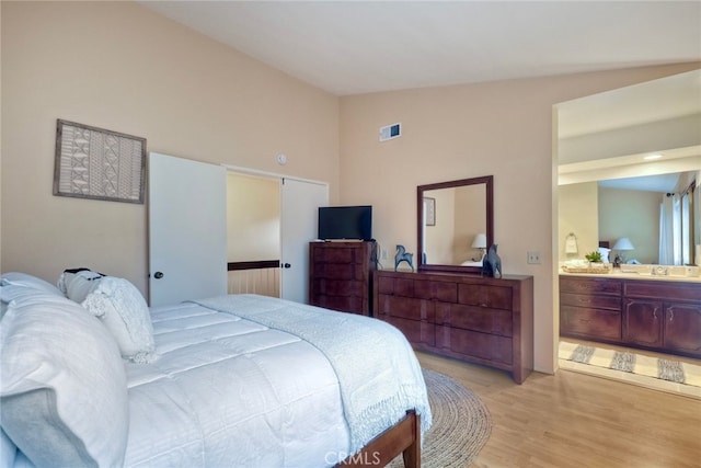 bedroom featuring lofted ceiling, light wood-type flooring, and ensuite bathroom