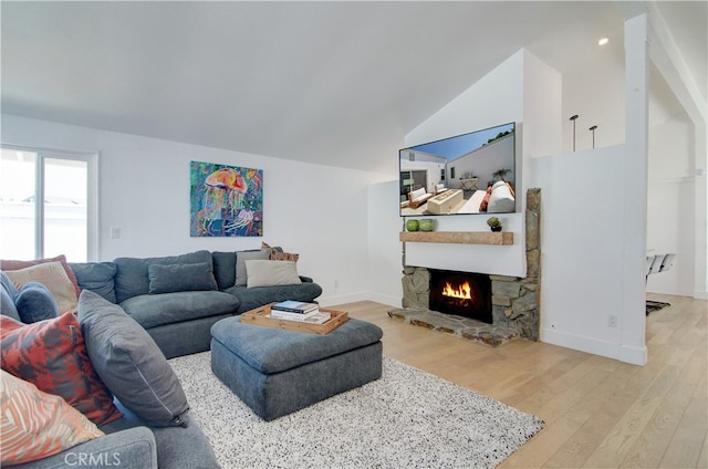 living room with light wood-type flooring, vaulted ceiling, and a stone fireplace