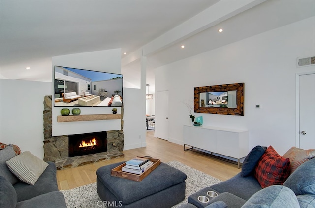 living room featuring light wood-type flooring, a fireplace, and beamed ceiling