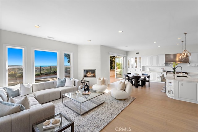 living room featuring a fireplace, light hardwood / wood-style flooring, a notable chandelier, and sink