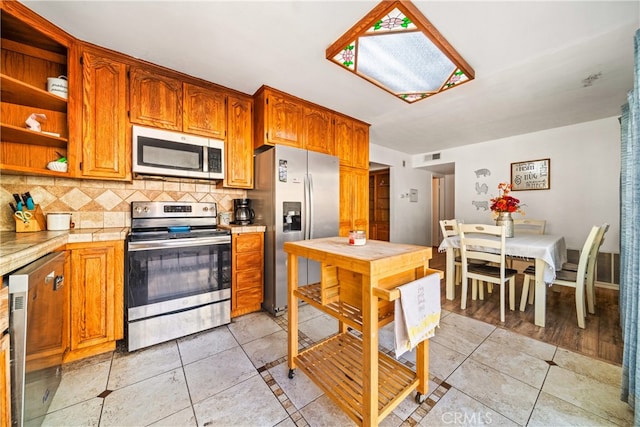 kitchen featuring stainless steel appliances, light tile patterned floors, tile counters, and tasteful backsplash