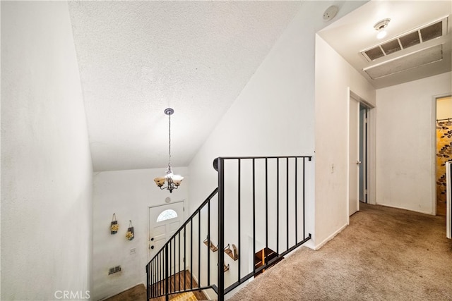 hall with lofted ceiling, a textured ceiling, carpet flooring, and an inviting chandelier