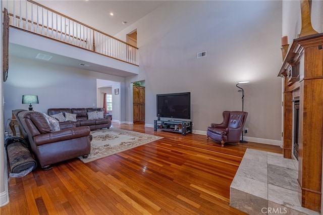 living room with a fireplace, a towering ceiling, and wood-type flooring