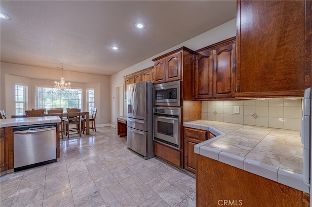 kitchen featuring a notable chandelier, tile counters, decorative backsplash, hanging light fixtures, and appliances with stainless steel finishes