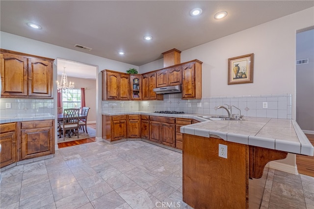 kitchen with gas stovetop, sink, kitchen peninsula, a chandelier, and tile counters