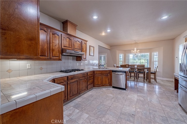 kitchen featuring backsplash, tile countertops, kitchen peninsula, hanging light fixtures, and appliances with stainless steel finishes