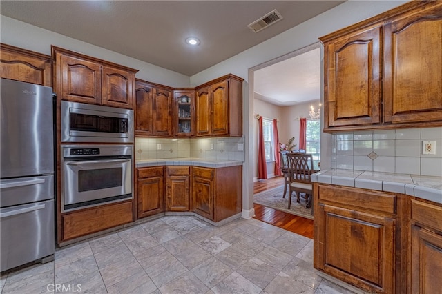 kitchen featuring light wood-type flooring, tasteful backsplash, a notable chandelier, appliances with stainless steel finishes, and tile counters