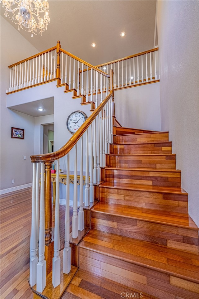 stairs with a towering ceiling, an inviting chandelier, and hardwood / wood-style flooring