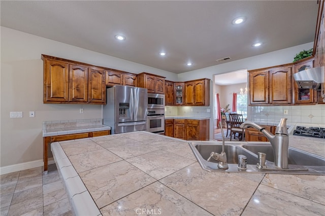 kitchen with sink, appliances with stainless steel finishes, tile counters, range hood, and backsplash