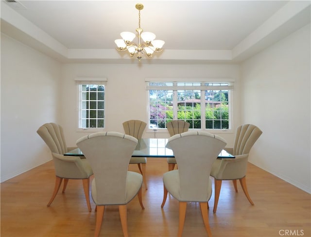 dining area featuring a notable chandelier, light hardwood / wood-style flooring, plenty of natural light, and a tray ceiling