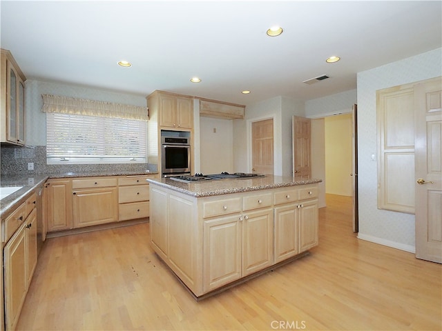 kitchen with light brown cabinets, stainless steel appliances, light hardwood / wood-style floors, and a center island