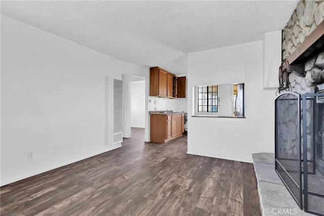 unfurnished living room with a stone fireplace, dark hardwood / wood-style flooring, and a textured ceiling