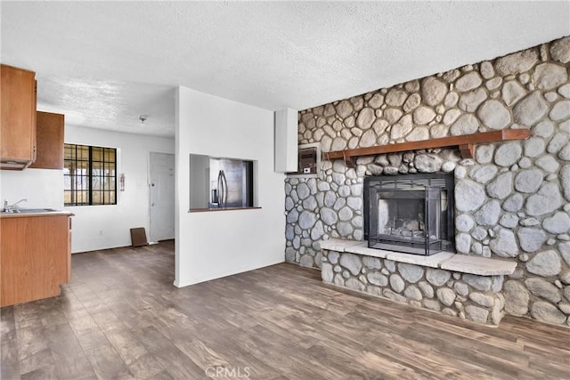 unfurnished living room featuring a fireplace, a textured ceiling, dark wood-type flooring, and sink