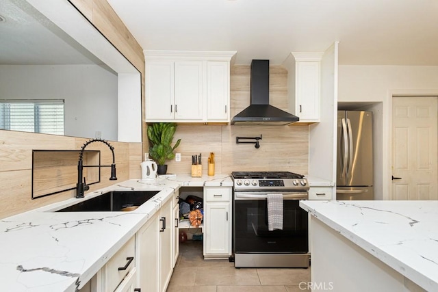 kitchen with appliances with stainless steel finishes, light stone counters, sink, wall chimney range hood, and white cabinetry