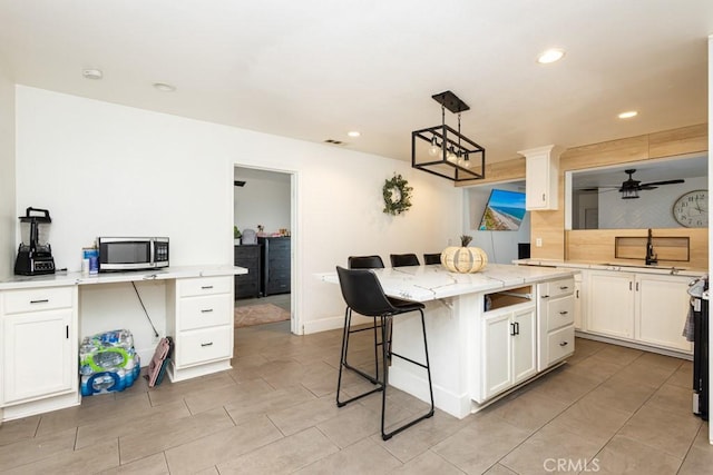 kitchen with ceiling fan, a kitchen breakfast bar, light stone counters, decorative light fixtures, and a kitchen island