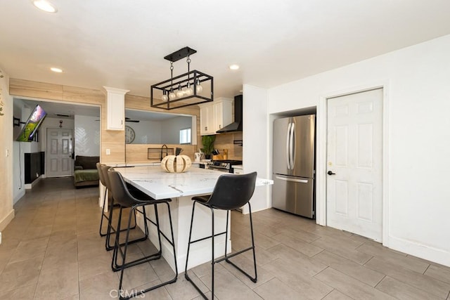 kitchen featuring backsplash, wall chimney exhaust hood, stainless steel fridge, decorative light fixtures, and a kitchen island