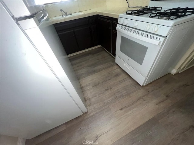 kitchen with tile counters, sink, white appliances, and light wood-type flooring