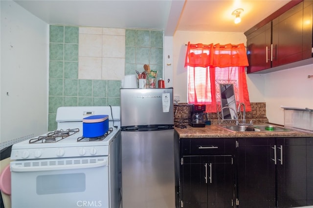 kitchen featuring stainless steel fridge, backsplash, tile walls, sink, and white gas range oven