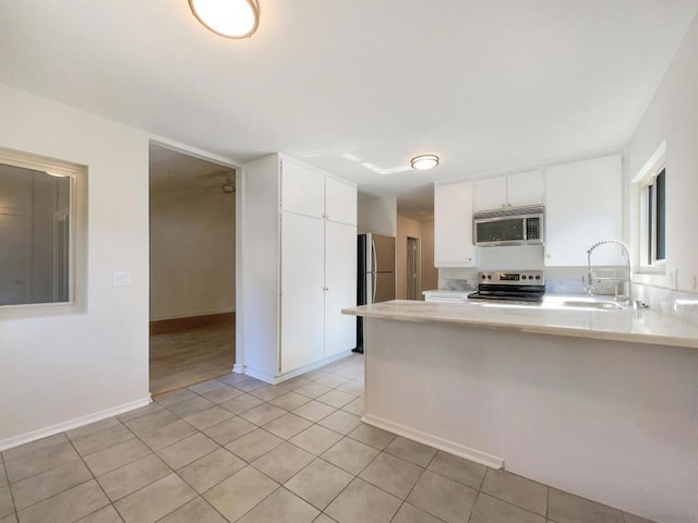 kitchen featuring kitchen peninsula, appliances with stainless steel finishes, sink, light tile patterned floors, and white cabinets