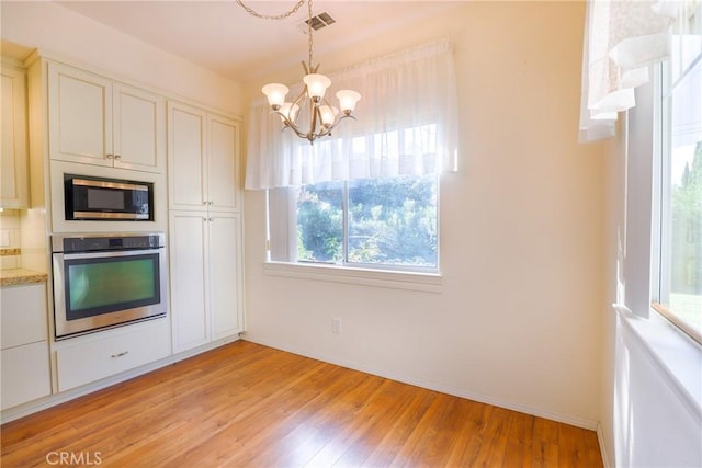 kitchen featuring hanging light fixtures, stainless steel appliances, light stone counters, a chandelier, and light wood-type flooring