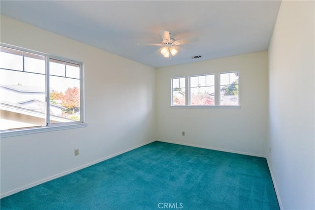 empty room with ceiling fan, a healthy amount of sunlight, and dark colored carpet