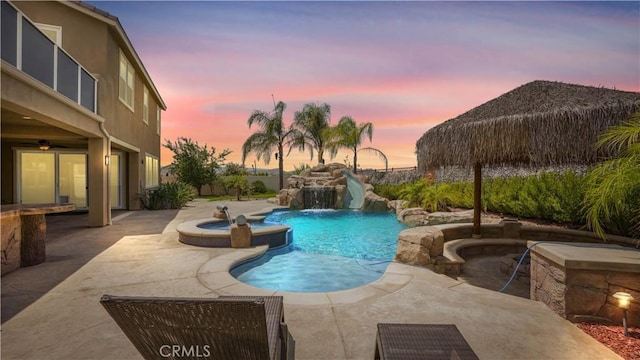 pool at dusk with an in ground hot tub, pool water feature, and a patio area