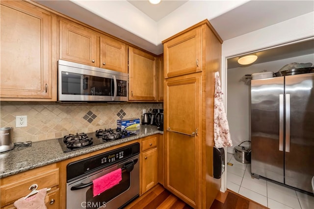 kitchen featuring dark wood-type flooring, stone countertops, appliances with stainless steel finishes, and backsplash