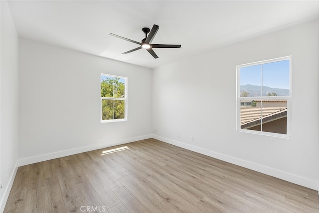 unfurnished room with ceiling fan, a mountain view, light hardwood / wood-style floors, and a wealth of natural light