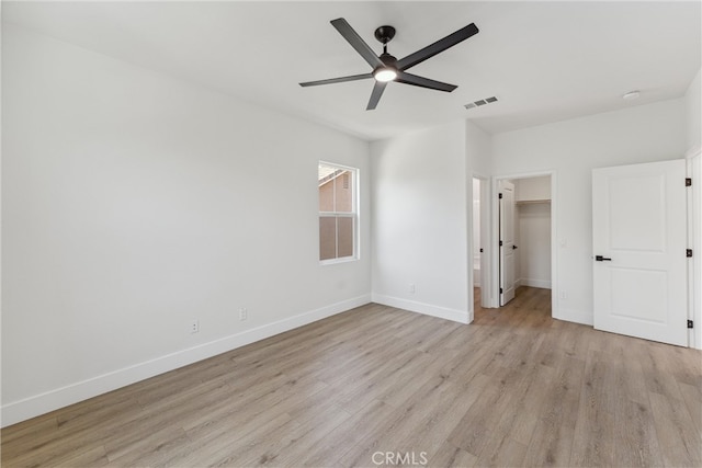 unfurnished bedroom featuring ceiling fan, a closet, light hardwood / wood-style floors, and a walk in closet