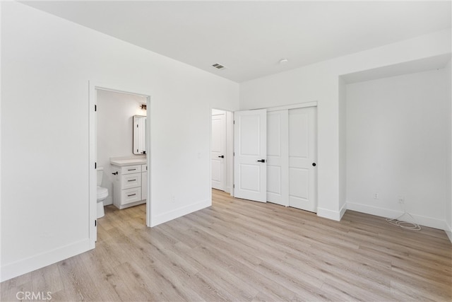 unfurnished bedroom featuring light hardwood / wood-style flooring, ensuite bath, and a closet