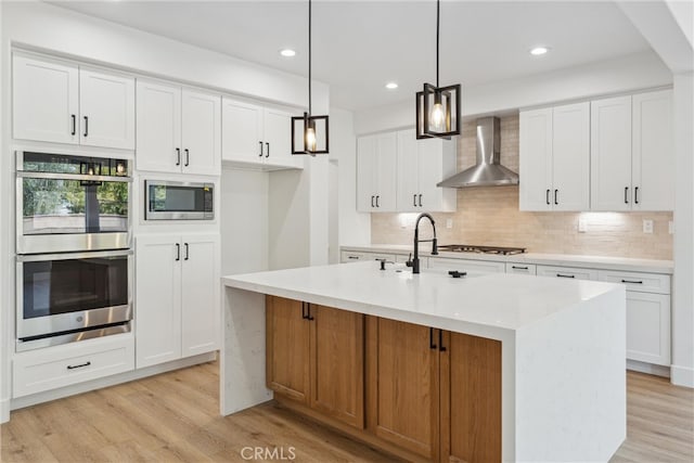 kitchen featuring white cabinets, a kitchen island with sink, and wall chimney range hood