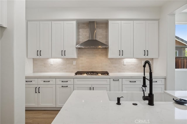 kitchen featuring stainless steel gas stovetop, white cabinets, decorative backsplash, and wall chimney range hood