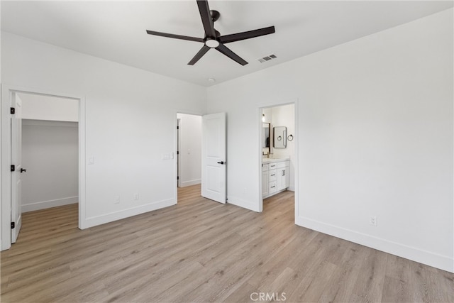 unfurnished bedroom featuring a closet, ensuite bath, light hardwood / wood-style floors, and a spacious closet