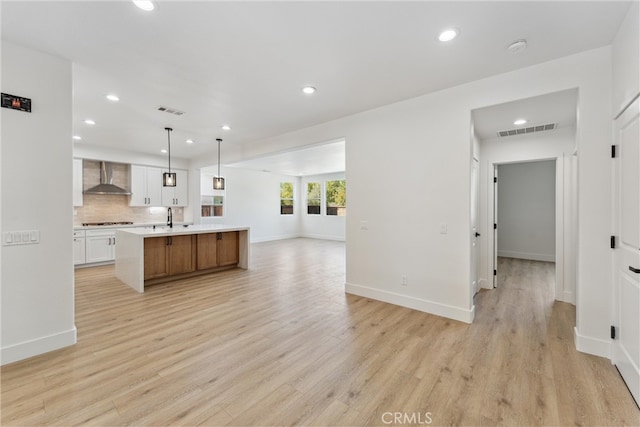 kitchen featuring a large island, white cabinets, hanging light fixtures, wall chimney range hood, and light hardwood / wood-style flooring