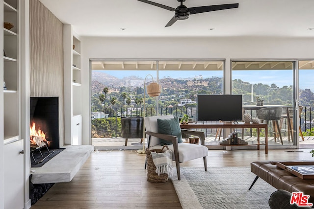 interior space featuring a large fireplace, built in features, ceiling fan, and dark wood-type flooring