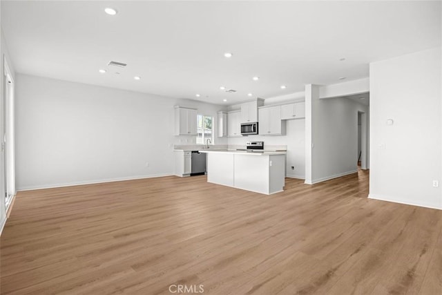 kitchen with white cabinetry, stainless steel appliances, light wood-type flooring, a kitchen island, and sink