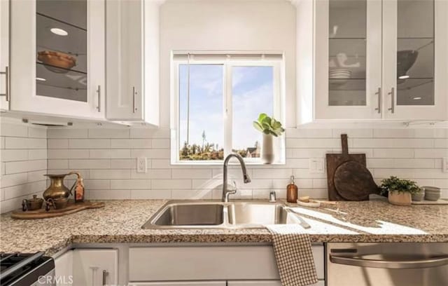 kitchen with tasteful backsplash, sink, white cabinetry, appliances with stainless steel finishes, and light stone countertops