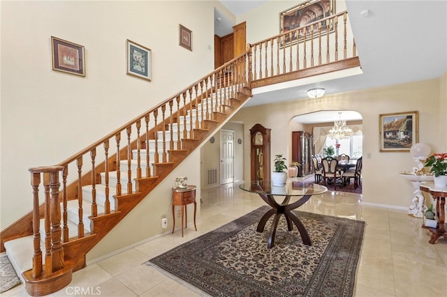 stairway featuring a towering ceiling, an inviting chandelier, and tile patterned flooring