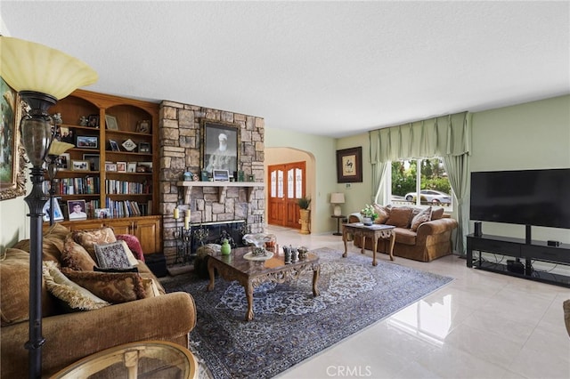 living room with a stone fireplace, a textured ceiling, and light tile patterned floors