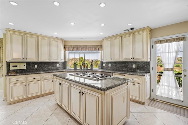 kitchen with cream cabinets, stainless steel gas stovetop, dark stone countertops, and a kitchen island