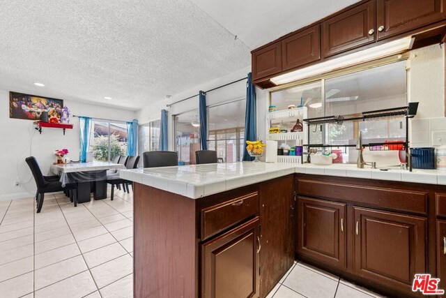 kitchen featuring sink, tile countertops, kitchen peninsula, light tile patterned floors, and a textured ceiling