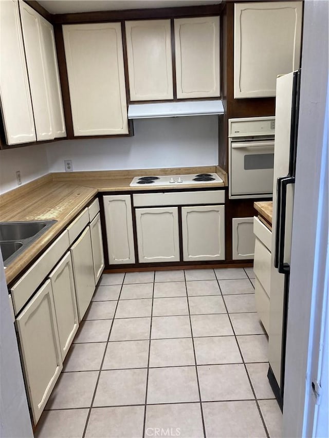 kitchen with white cabinets, light tile patterned floors, white appliances, and sink