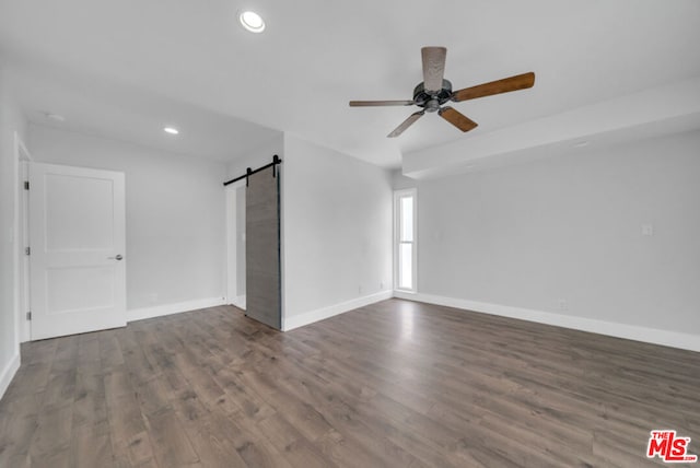 unfurnished room featuring ceiling fan, dark wood-type flooring, and a barn door