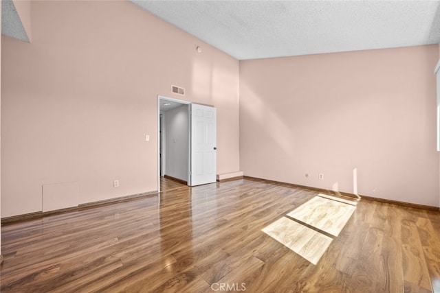 empty room with a textured ceiling, hardwood / wood-style floors, and high vaulted ceiling